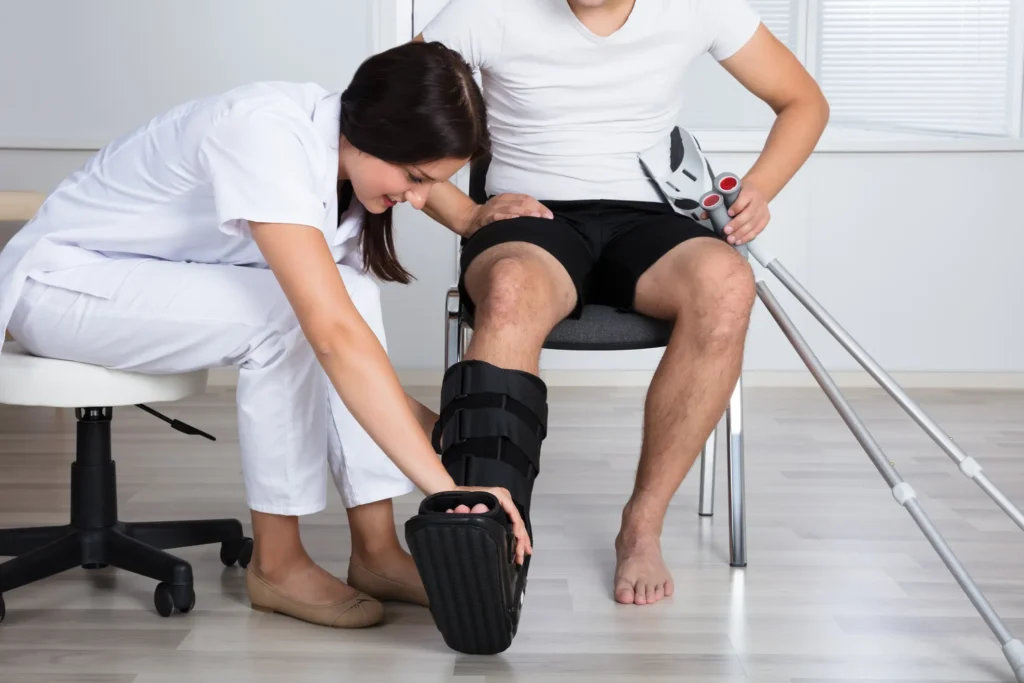 Young Female Doctor Putting Walking Brace On Person's Leg In Hospital